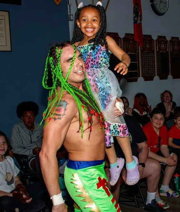 A young fan is thrilled to be carried by her favorite, CWE star CAM!!ikaze. Photo by Mark Whatman